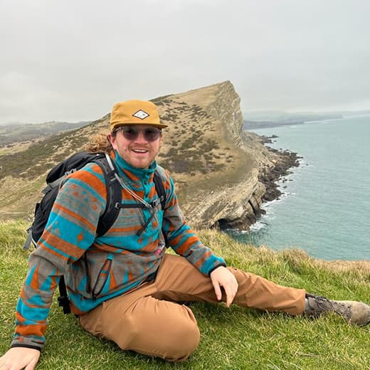 James Newton sitting on a grassy cliff overlooking the coast